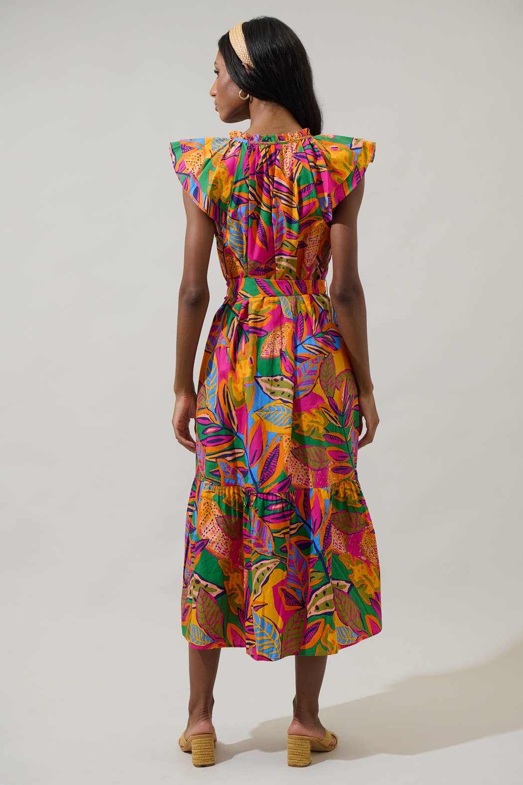model in a midi length tropical print dress with a ruffled neckline and buttons at the center front