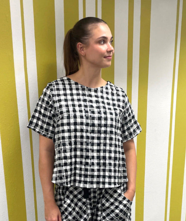 model in a short sleeve black and white plaid boxy tee, with a matching wide leg pant with long exterior pockets and a tapered ankle