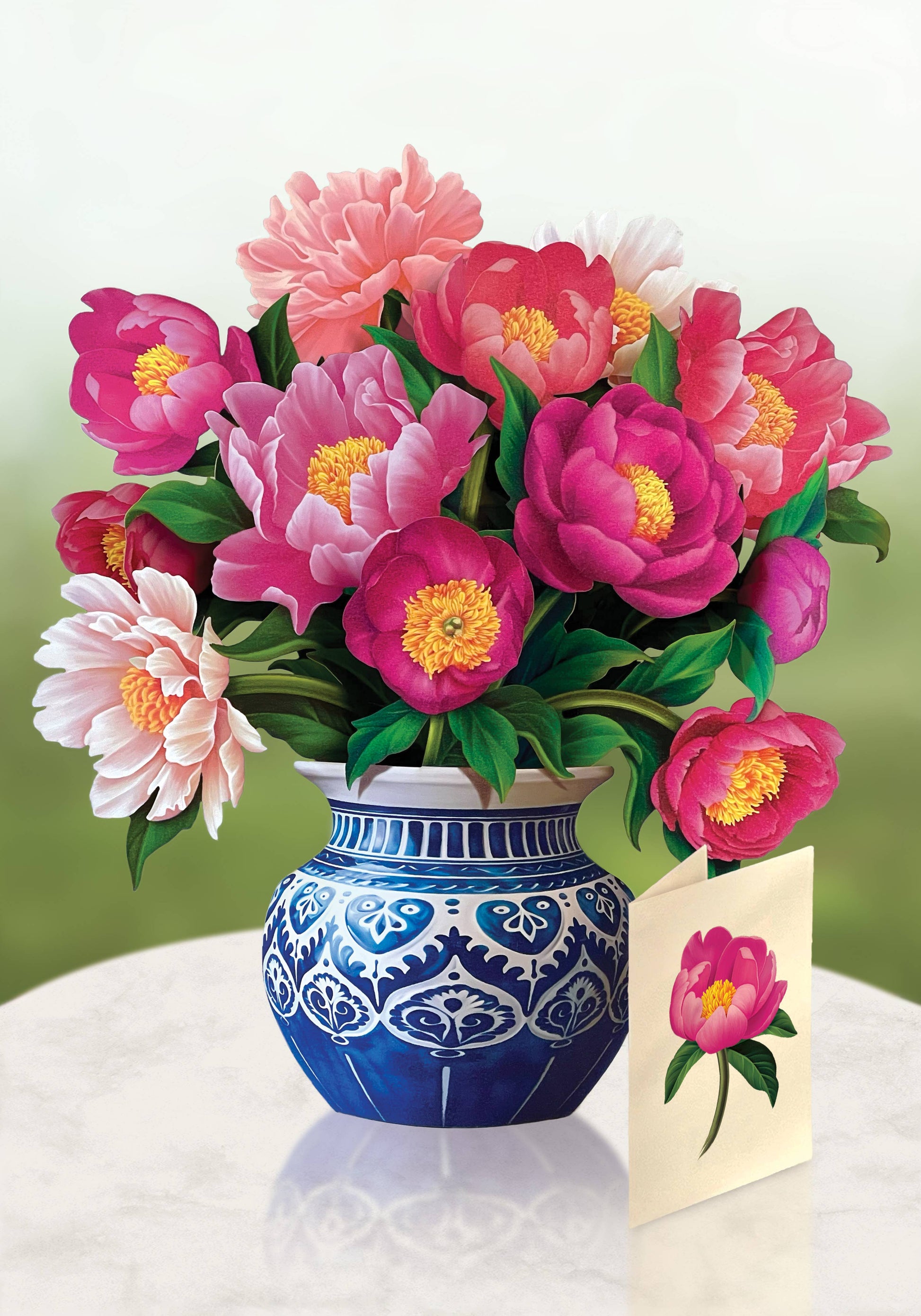 Bouquet of pink flowers in a blue and white vase with a matching card on a white surface.