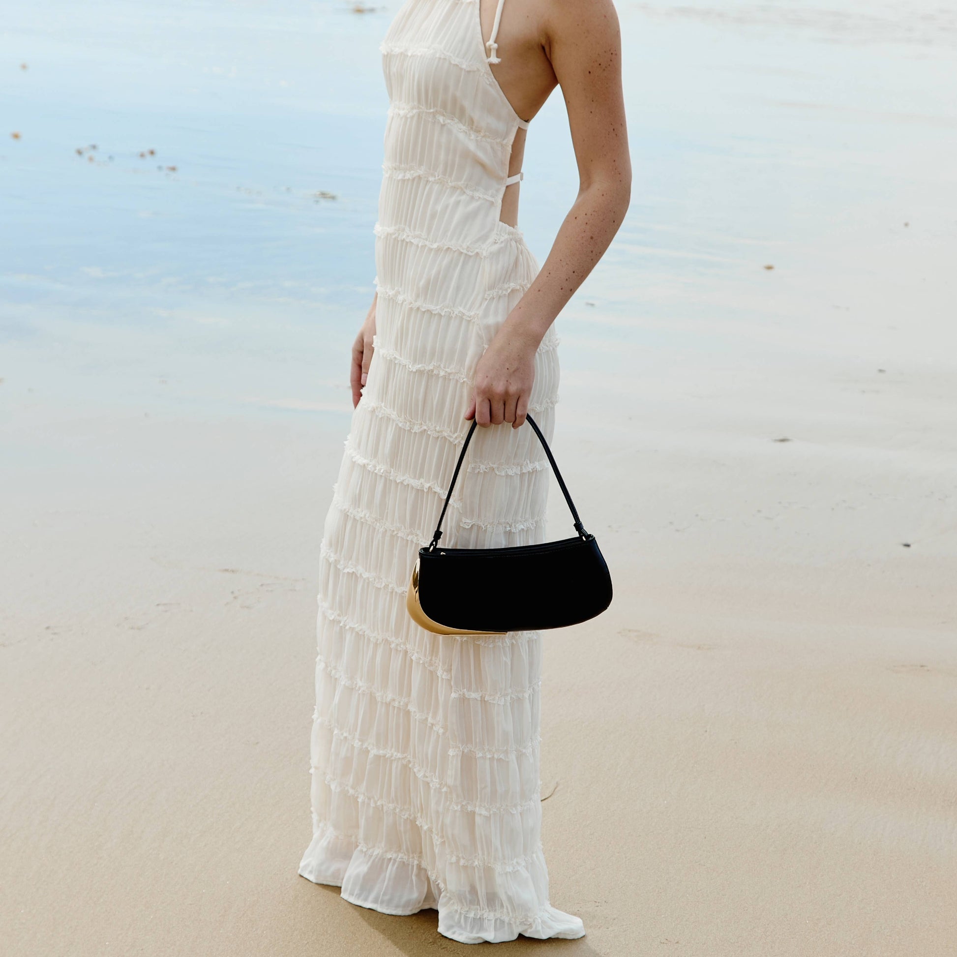 Woman in a white dress holding a black handbag on a beach