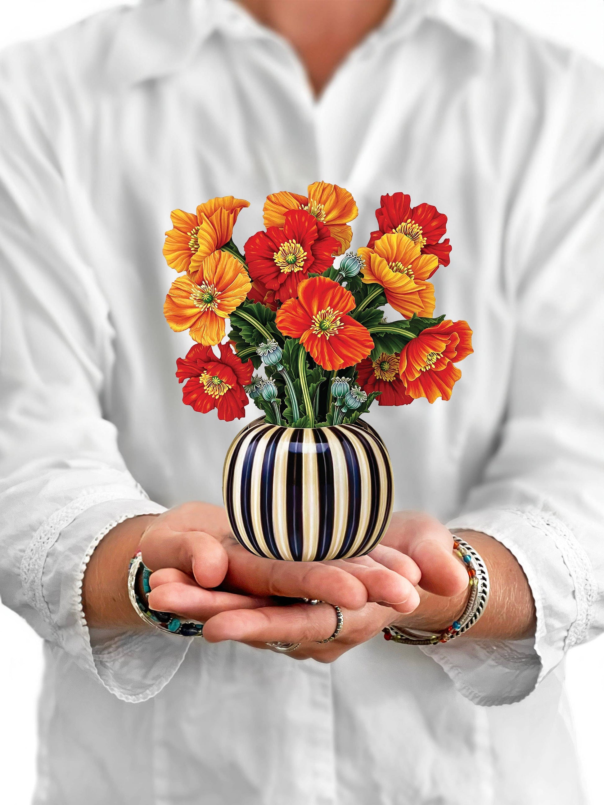 Person holding a striped vase with colorful flowers against a white background