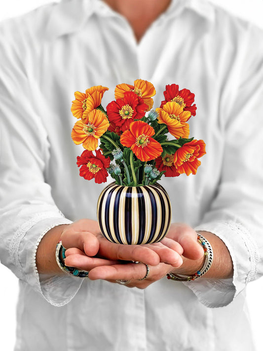 Person holding a striped vase with colorful flowers against a white background