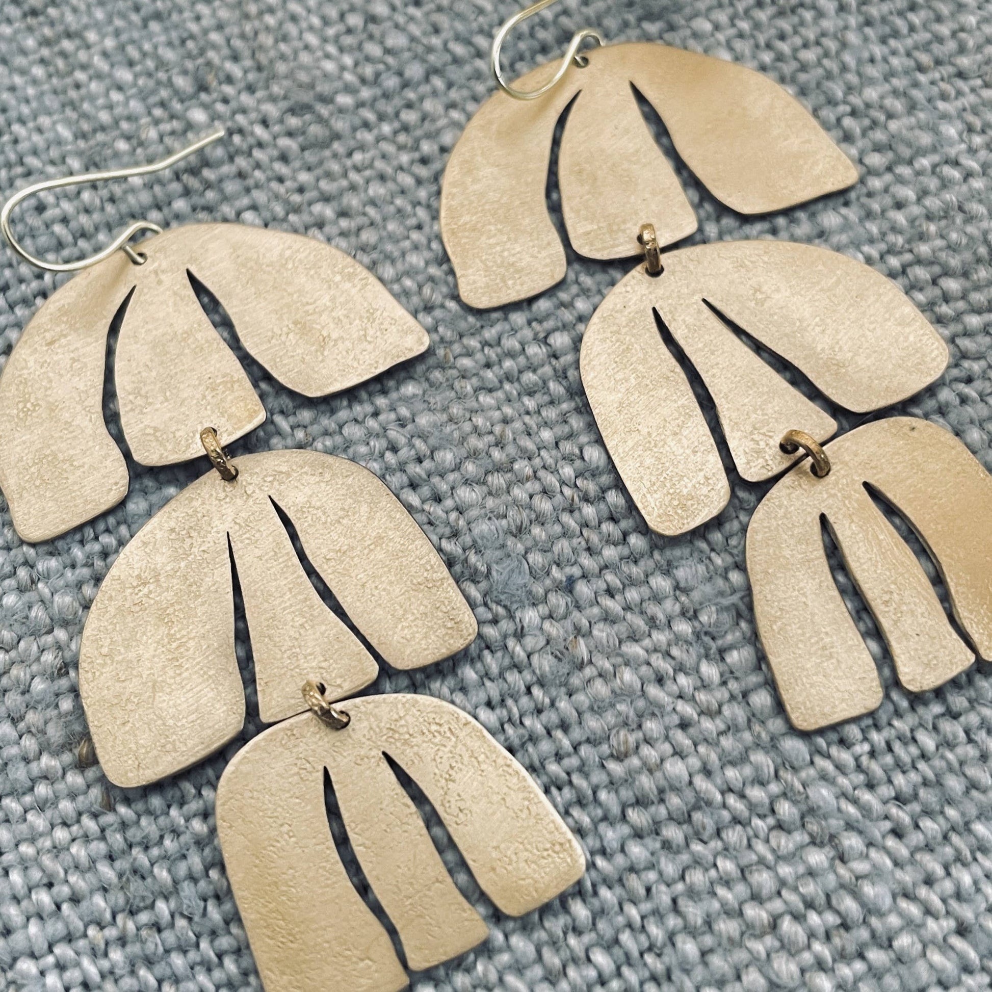 Pair of gold leaf-shaped earrings on a textured gray surface