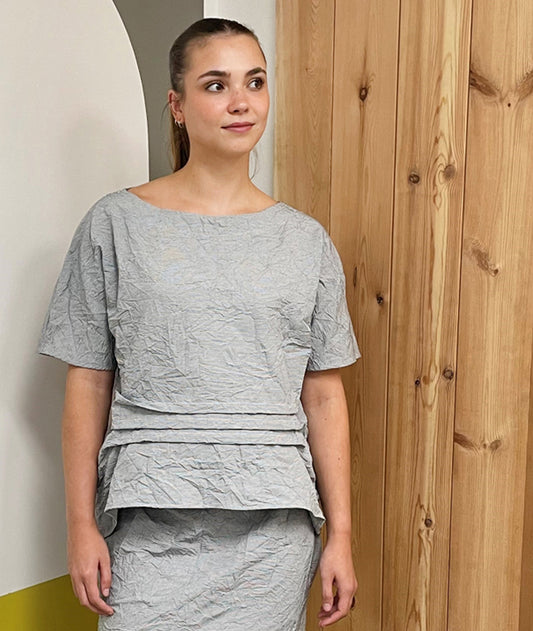 model in a grey and white pinstripe skirt and top with a crush texture. top and skirt both have horizontal tucks above the front center hems