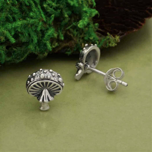 Silver mushroom-shaped earrings on a green surface with a leafy background