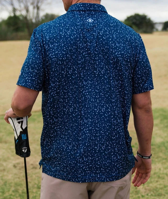 model wearing navy speckled polo with hat and shorts at golf course