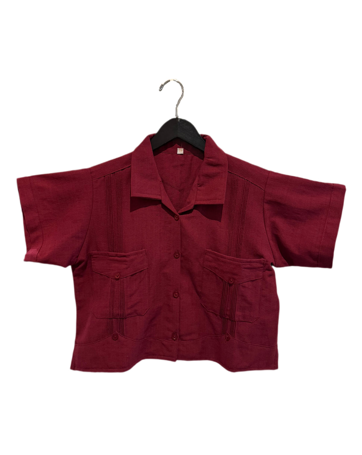 A short-sleeve button-up shirt in deep burgundy, hanging on a black hanger against a plain white background. The shirt features vertical pleats on the chest and waist, and two front flap pockets.