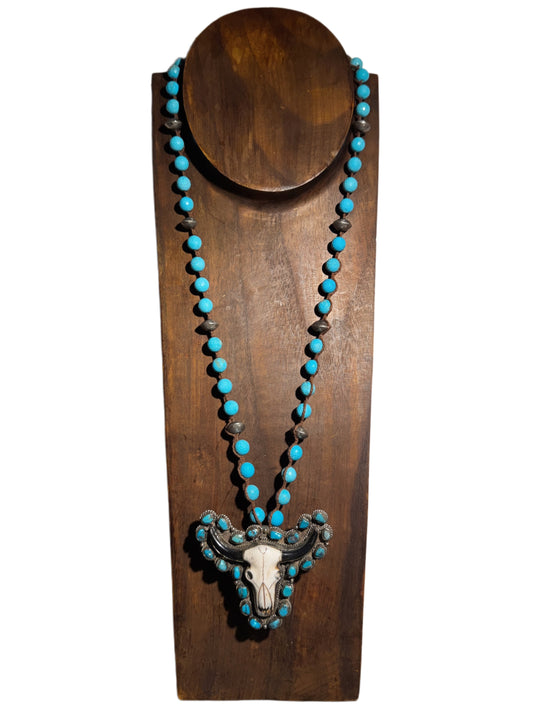Turquoise beaded necklace with a skull pendant on a wooden stand