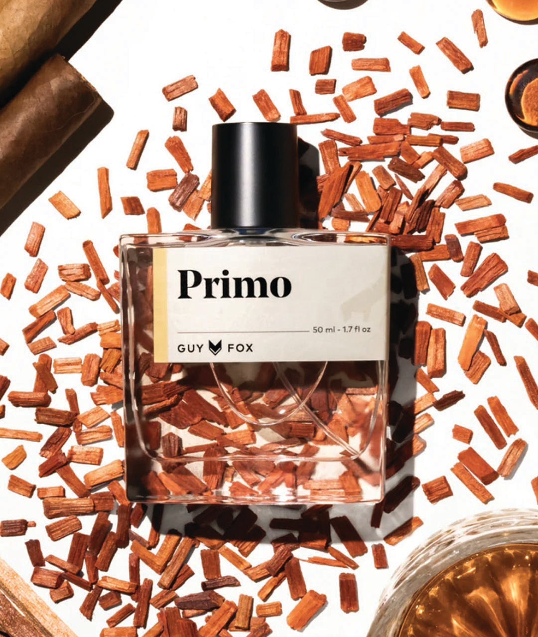 Primo Guy Fox perfume bottle surrounded by cinnamon sticks and other spices on a white background