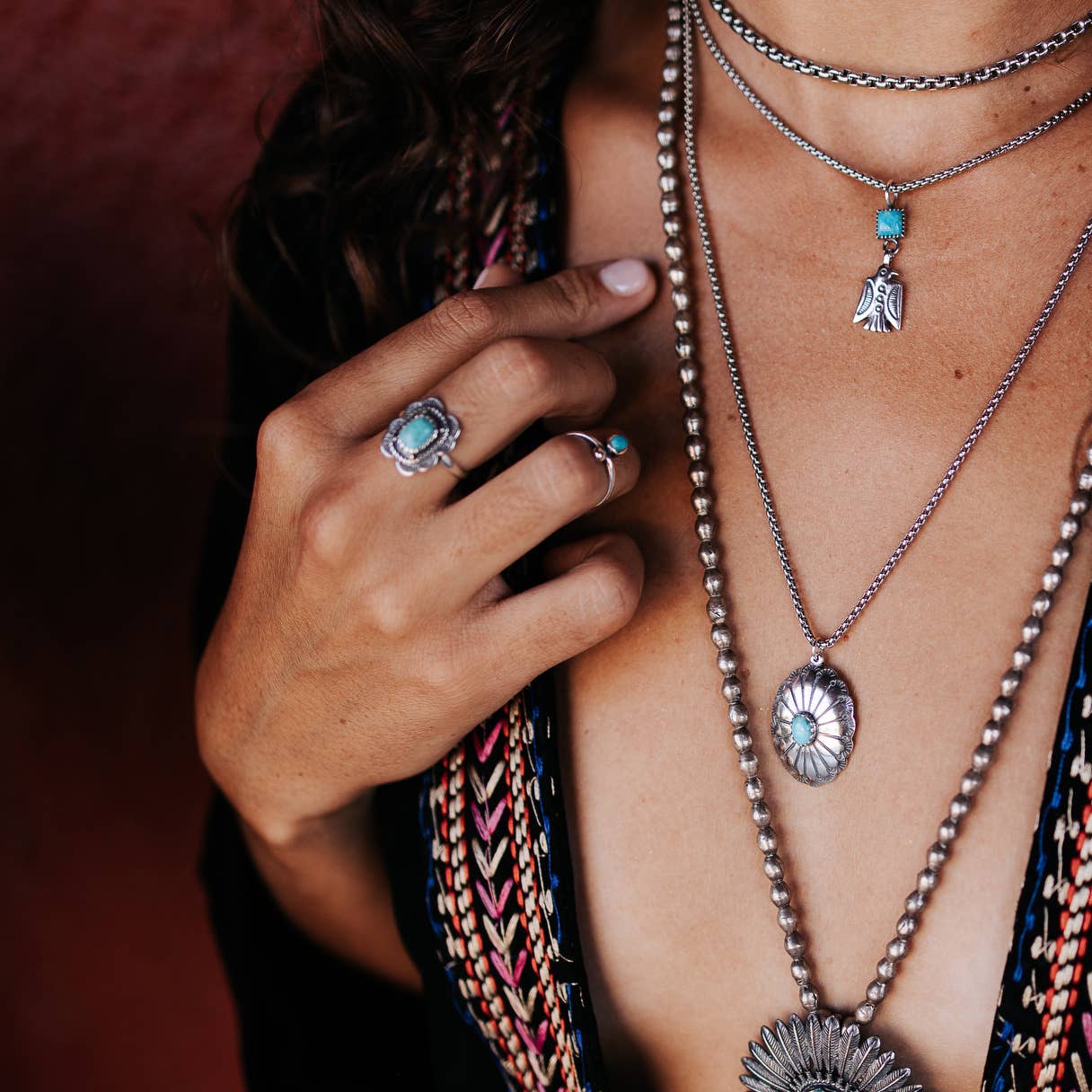 Close-up of layered necklaces and rings with turquoise stones on a blurred background