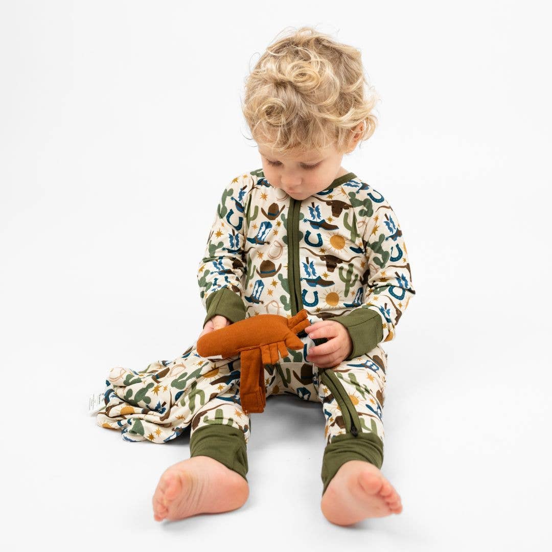 Child wearing a patterned onesie holding a toy on a white background