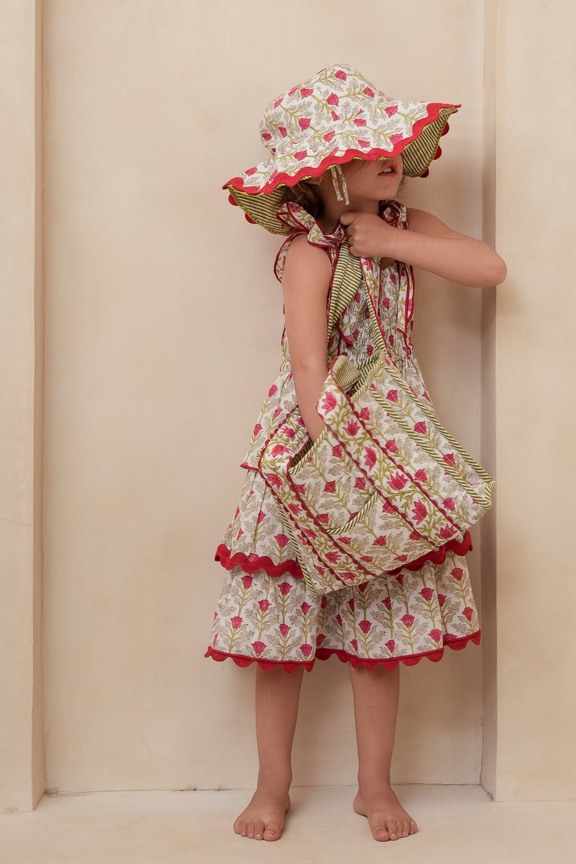Child wearing a floral dress and hat against a beige wall