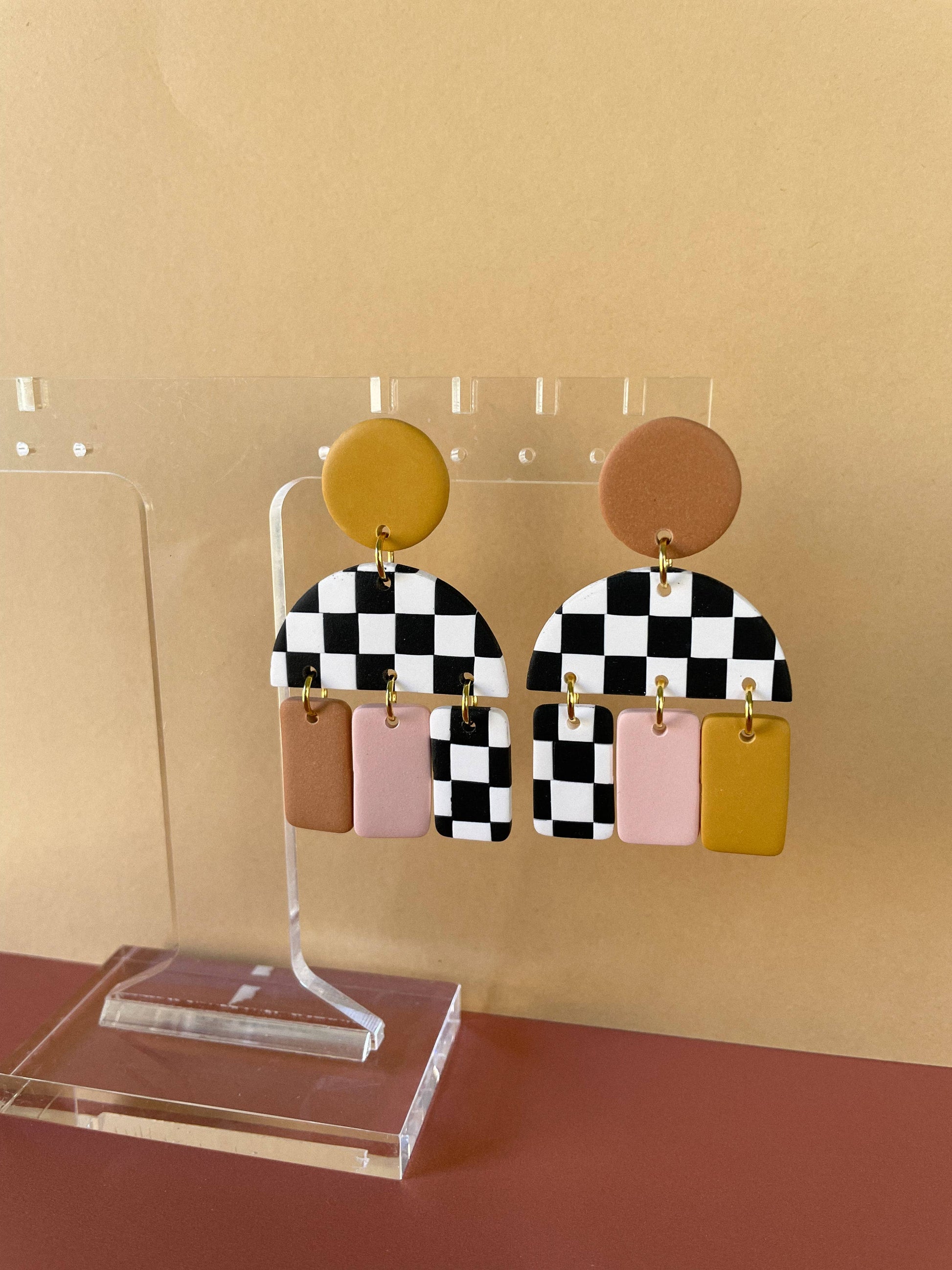 Post dangle earrings with checkered base and warm pops of color. circle, semi circle and rectangle drops. on light yellow and dark brick background