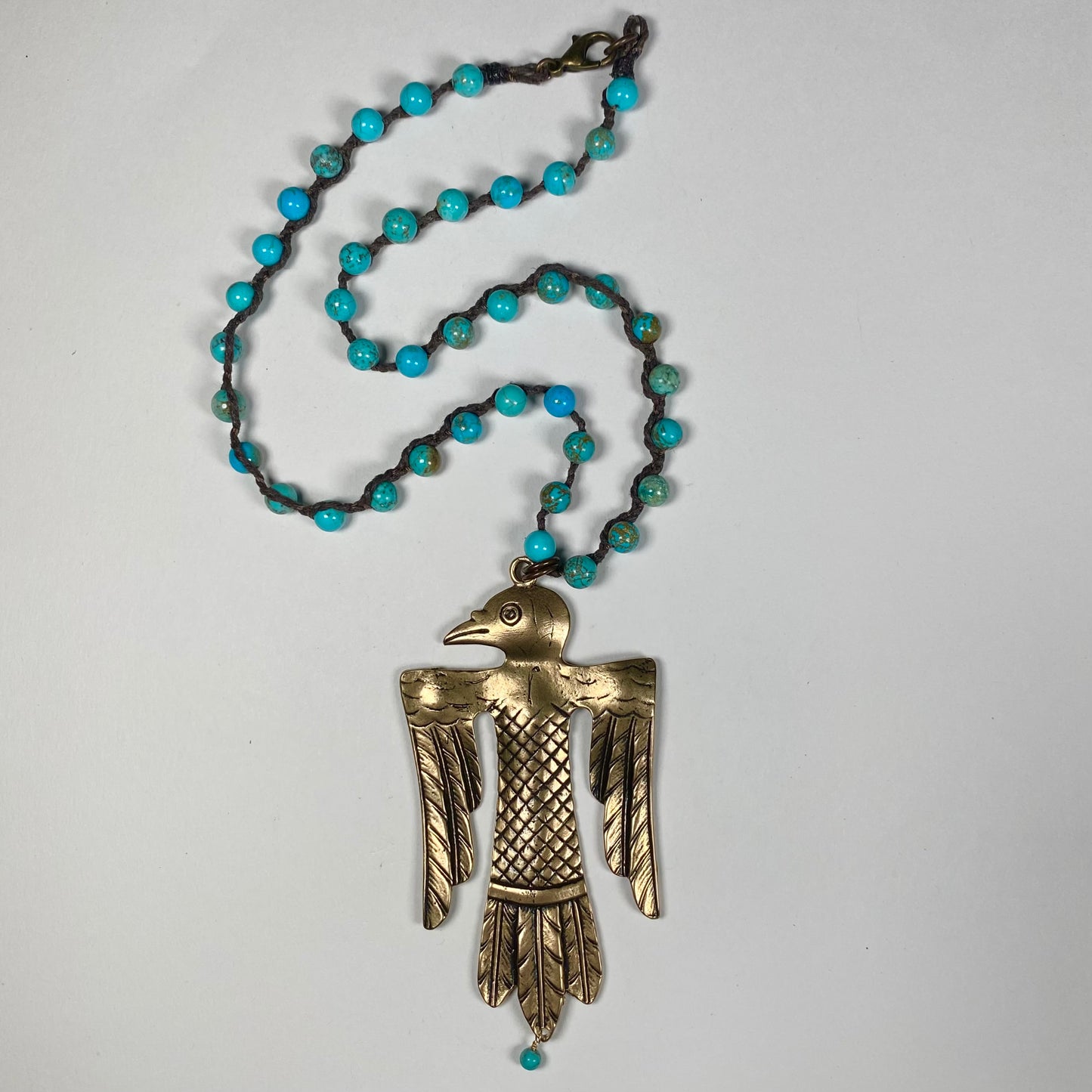 an engraved Bronze Thunderbird pendant featuring dangling Turquoise bead on a necklace strand of Turquoise beads.