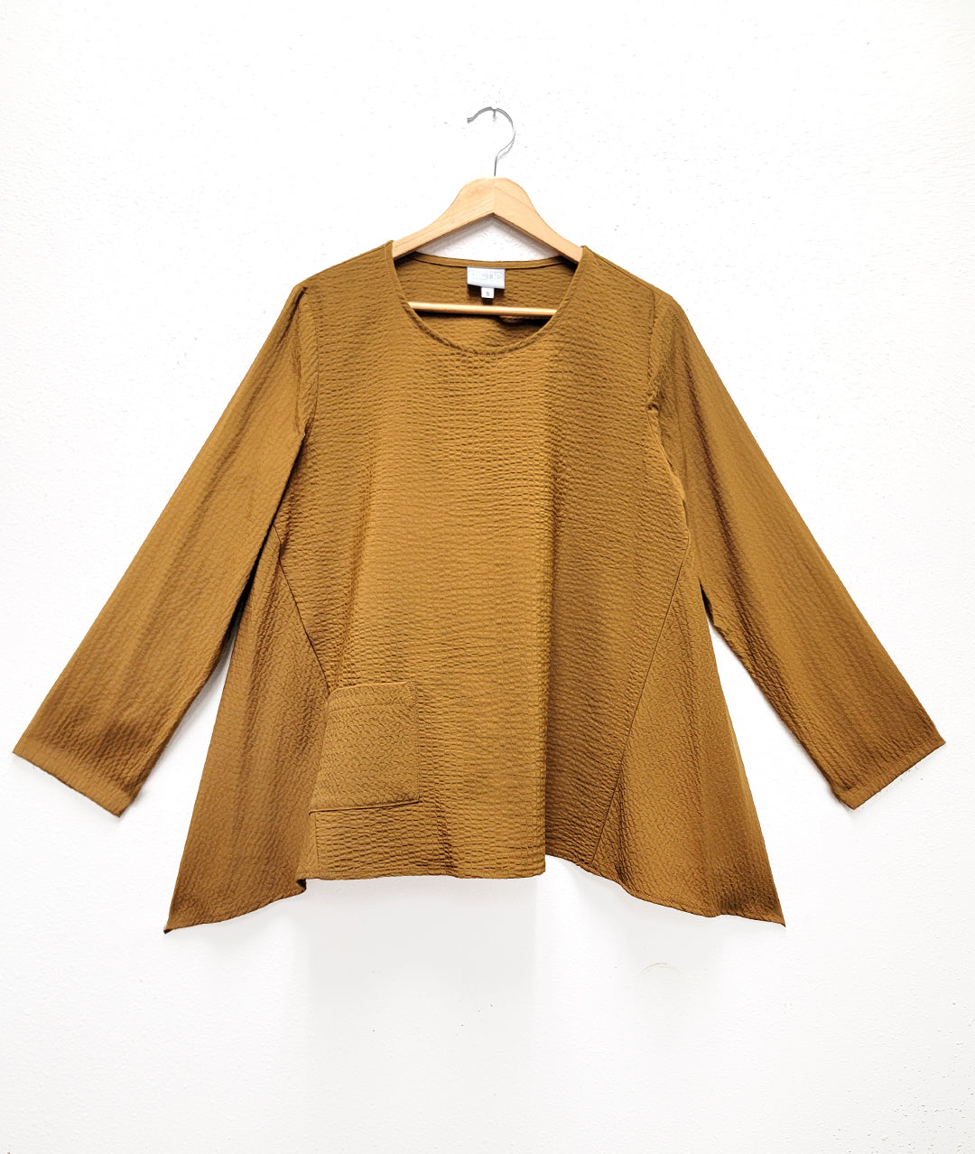 dijon yellow color pull over top with a single squared hip pocket, long sleeves and a hankerchief hemline