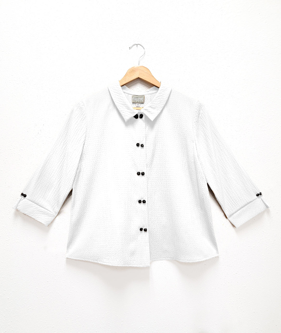 white, seersucker textured top with double sets of "twin" shell buttons down the front, easy a-line shape and straight hem. 3/4 length sleeves, with inverted pleat and open notched collar in back.