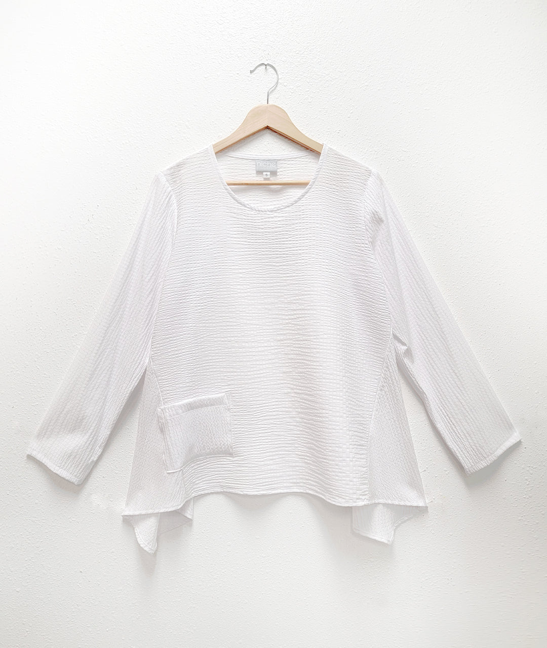 white pull over top with a single squared hip pocket, long sleeves and a hankerchief hemline