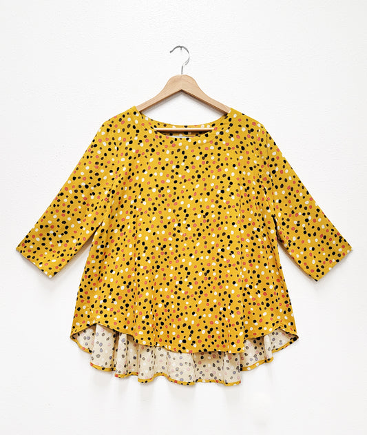 mustard yellow pullover top with a multi color polkdot print. top has 3/4 sleeves, round neckline, high-low hem with a full flowy body