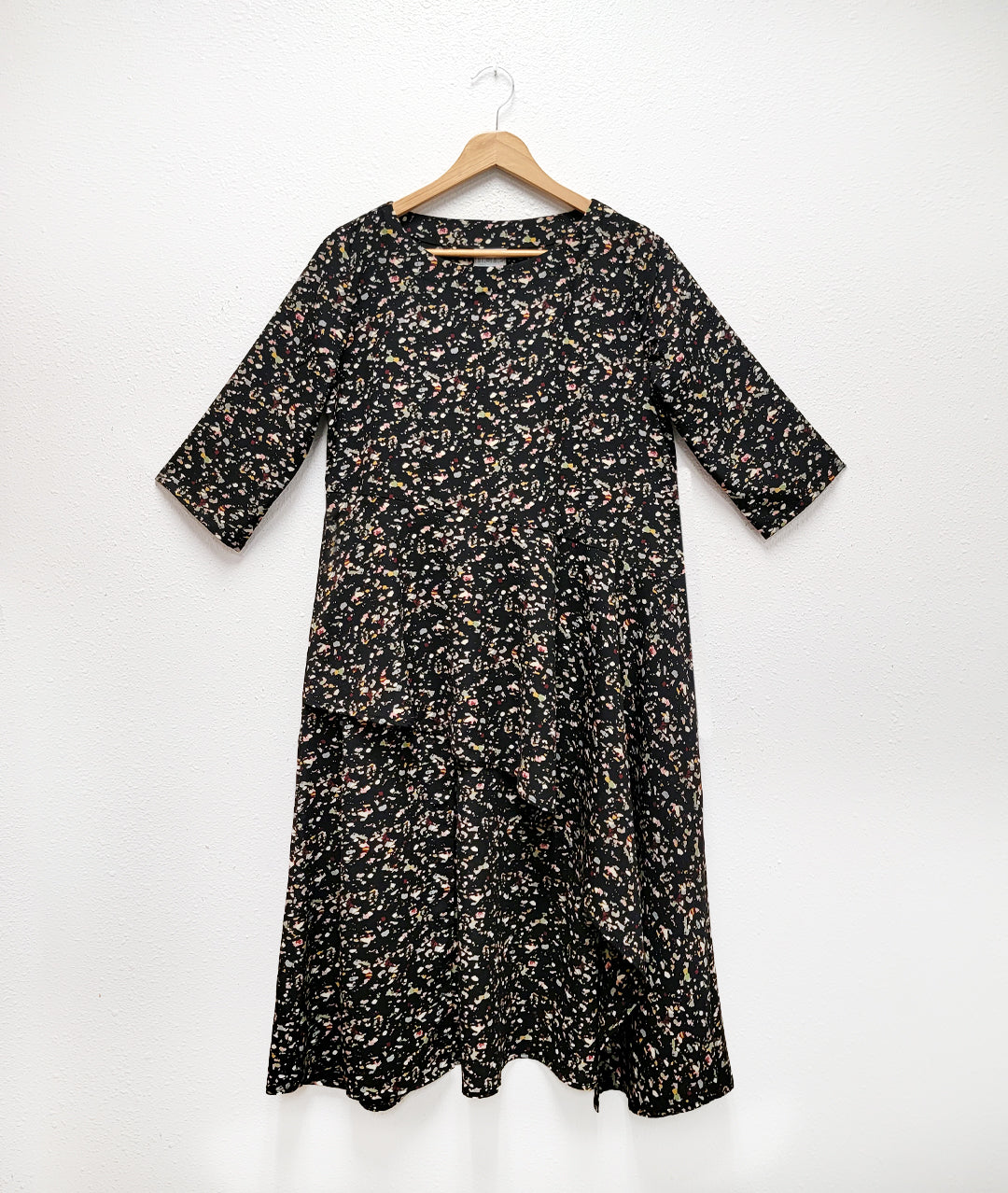 black terrazzo print tunic with elbow length sleeves and an asymmetrical waist and skirt, with a short front and long sides and back. pockets set into side seams