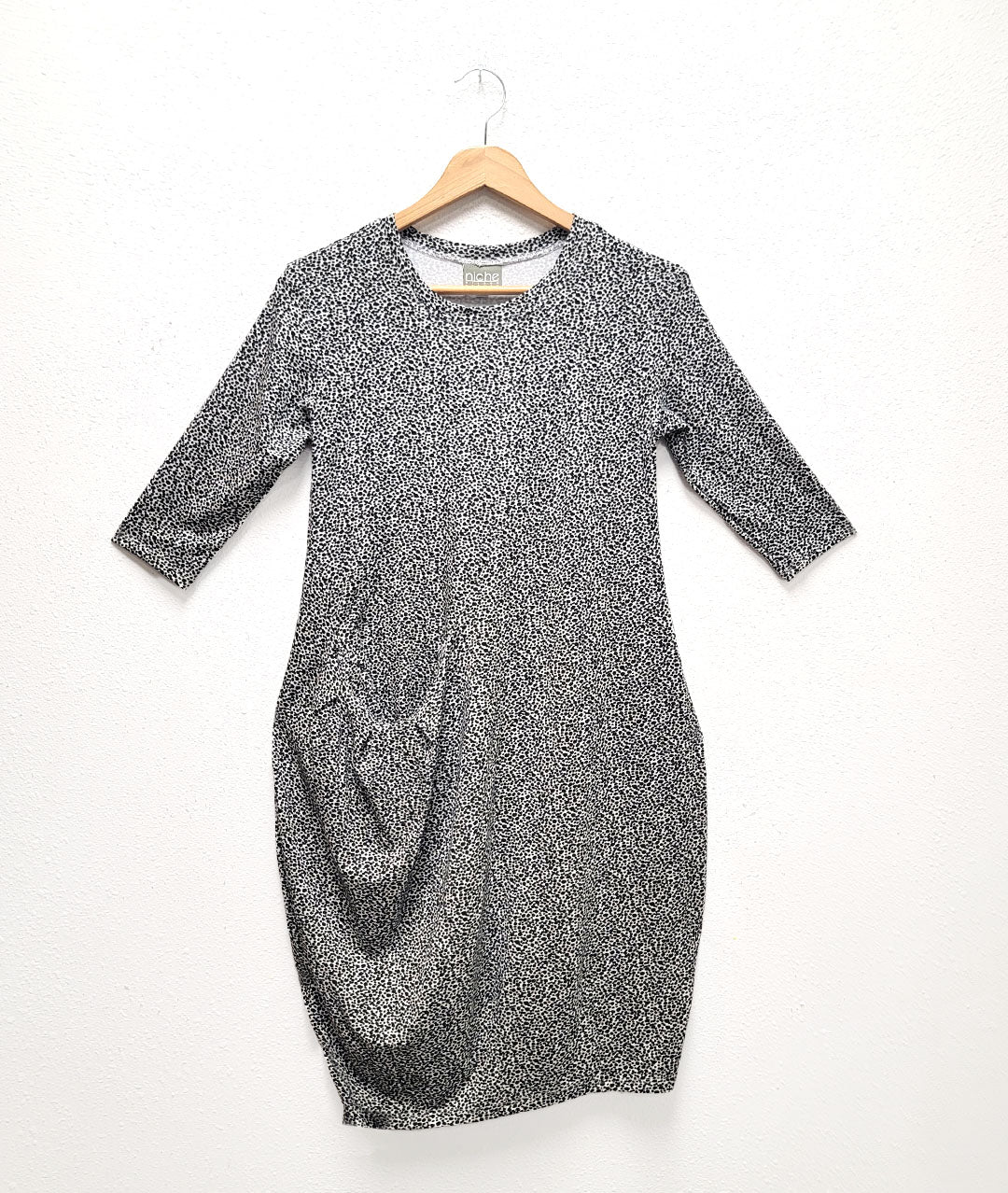 black and white speckle print pullover tunic with a black dot print. dress has an asymmetrical seam across the front body with a curved pocket set into a seam at the hip. dress is knee lengh and has 3/4 sleeves and a round neckline