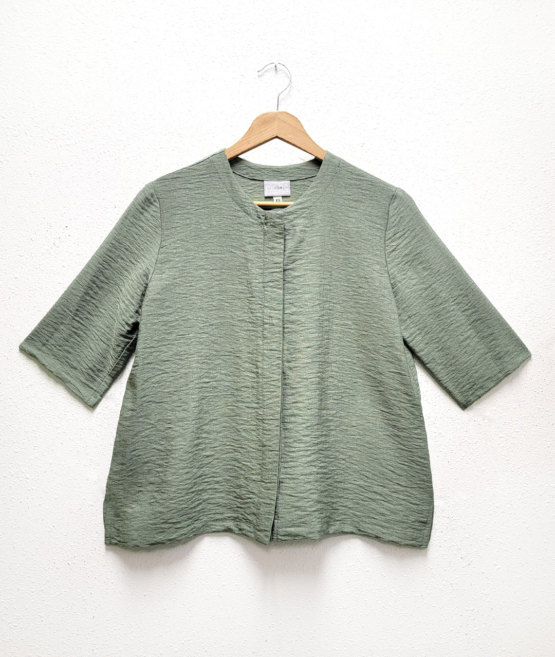 moss green top with 3/4 sleeves, a small slit on either side hem, a round neckline and buttons under a hidden placket
