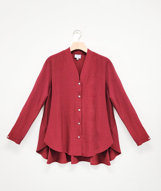 deep red button down blouse with long sleeves and a flowy, full back. top has a button at each wrist and a deep neckline with a standing collar