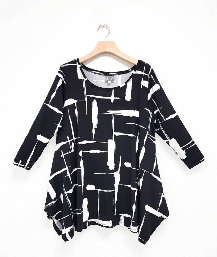 black and white print pullover top with a round neckline, 3/4 sleeves, and a wide hem with splits on either side, giving the illusion of a dipped hem