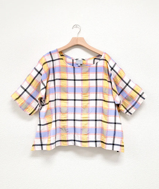 boxy and short top with dolman sleeves and a no shoulder seam in a plaid pastel pattern on hanger with white background
