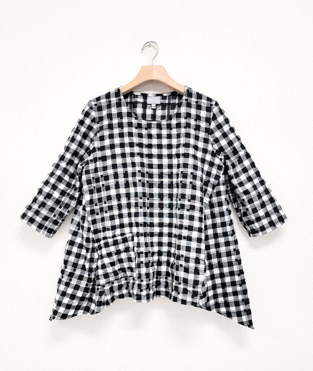 black and white plaid pull over top with 3/4 sleeves, dipped hem on either side, and a single square hip pocket