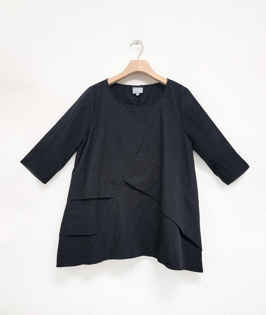 black pullover top with an asymmetrical tuck and seam detail across the body. top has 3/4 sleeves