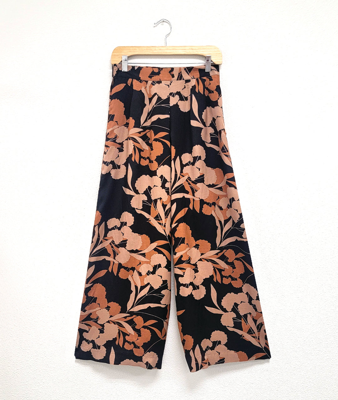 wide leg black palazzo pant with a floral and leaf silhouette print in different shades of orange. elastic waist in back and a flat waist in front with darts for shape