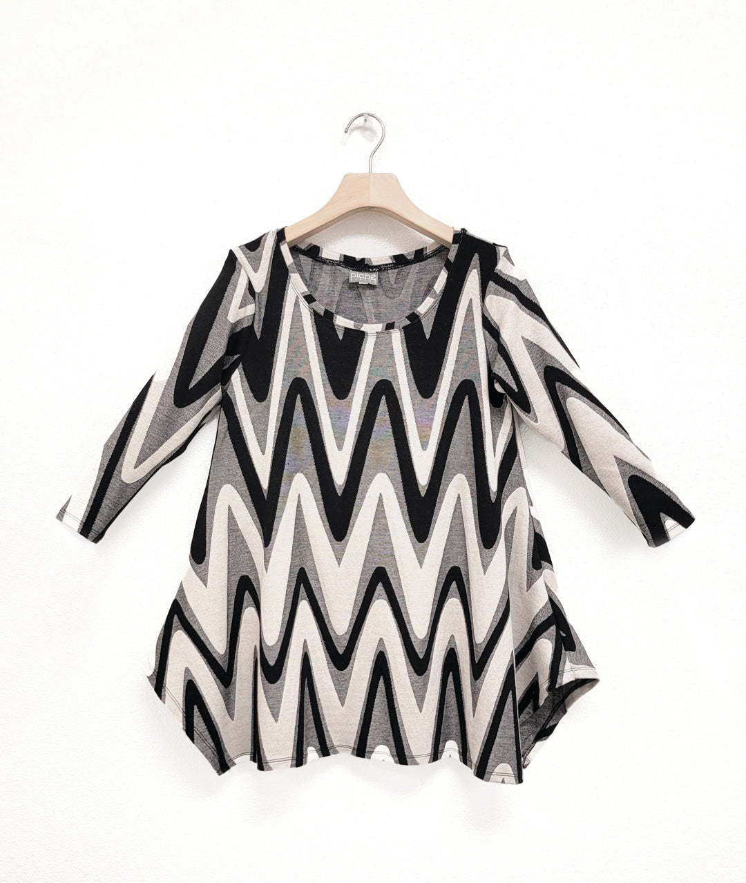 black, ivory and grey zigzag print pullover top with a round neckline, 3/4 sleeves, and a wide hem with splits on either side, giving the illusion of a dipped hem