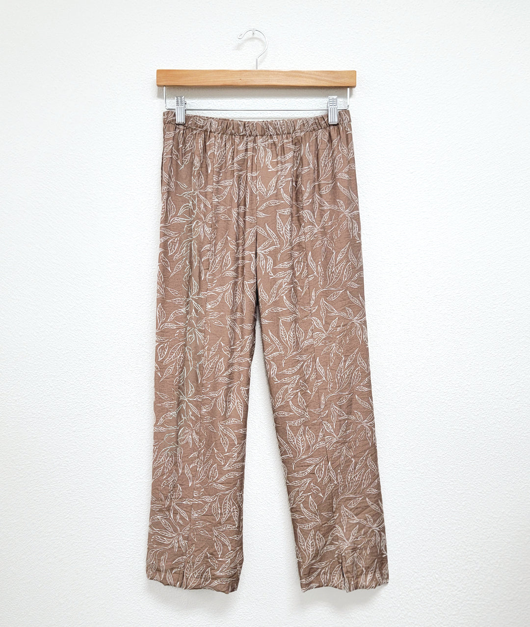 straight leg taupe pant with a white leaf print. elastic waistband and a center front seam on each leg with a small split at the hem