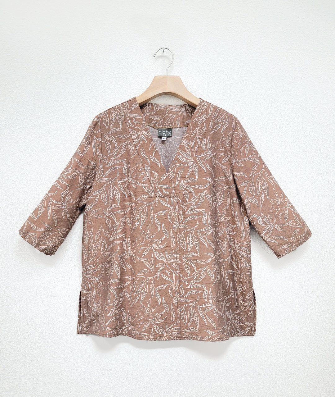 taupe leaf print  top with a white leaf print. top has a vneck and 3/4 sleeves and a center front seam and splits on either side.