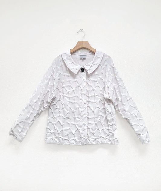 white blouse in a puckered dot texture. blouse has long sleeves, a collar, a hidden placket with snaps and a single large button at the top center