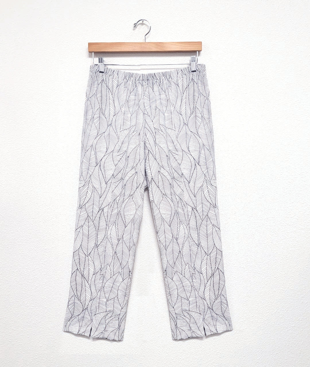 white straight leg pant with an elastic waistband, a split at each ankle front, and a grey leaf print all over the pant