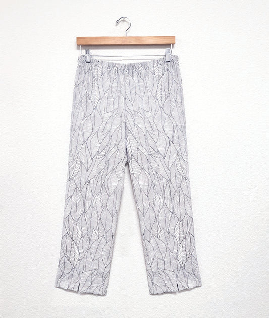 white straight leg pant with an elastic waistband, a split at each ankle front, and a grey leaf print all over the pant