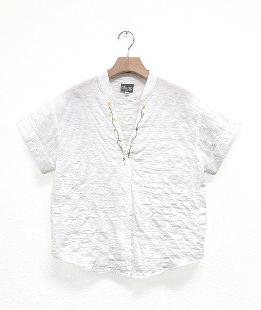 WHITE TEXTURED SHIRT WITH A V-NECK, CUFFED SLEEVES AND A SMALL STANDING COLLAR. floral embroidery at the v-neck, small dots at the sleeve cuffs