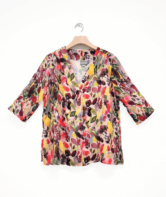 Colorful floral blouse with half sleeves and v-neck on a hanger against a white background
