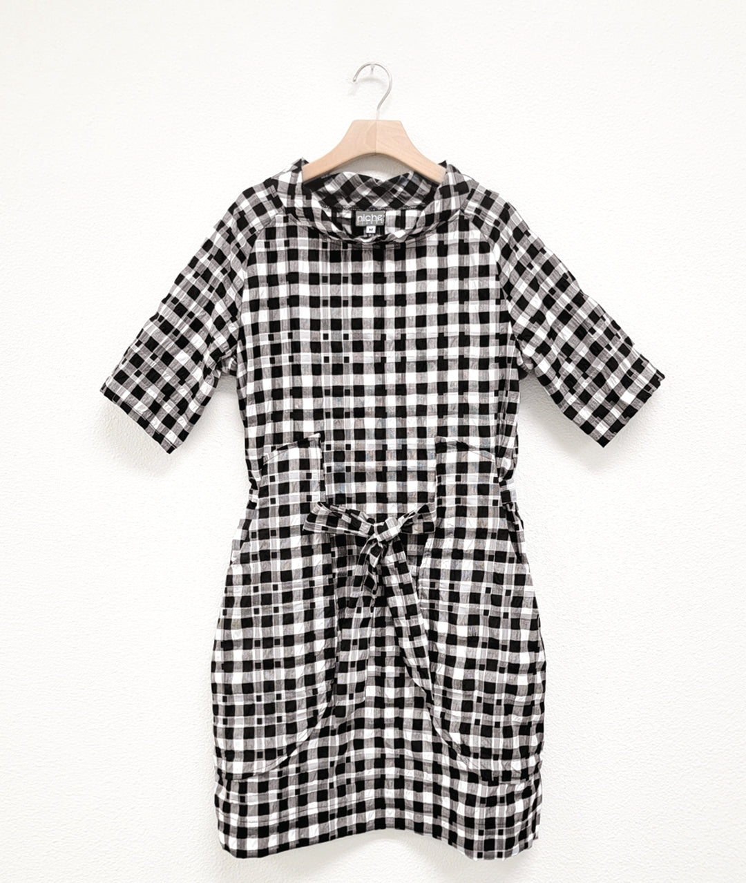 black and white plaid raglan sleeve shift dress with a matching tie belt at the waist, which runs through exterior pocket loops