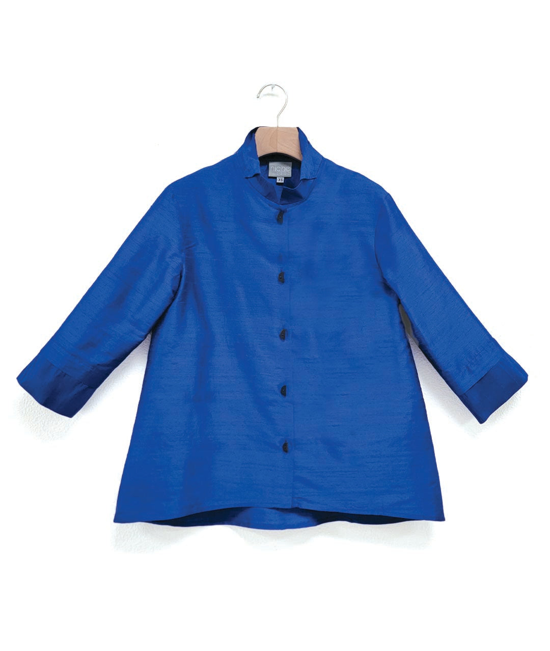 blue dupioni silk blouse with black half-moon buttons, a wide cuff on a 3/4 sleeve, and a double collar. blouse has a lower hem in the back.