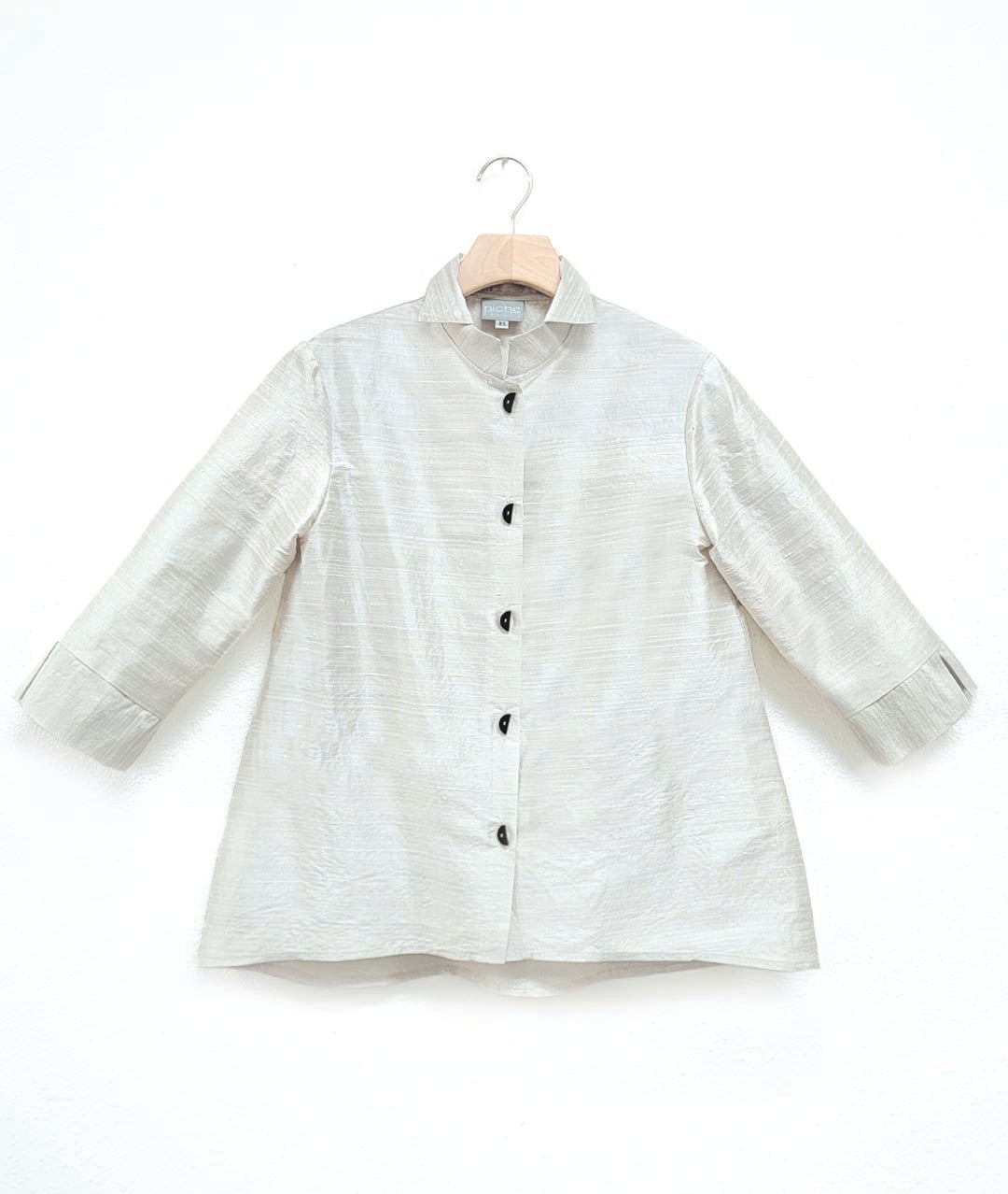 white dupioni silk blouse with black half-moon buttons, a wide cuff on a 3/4 sleeve, and a double collar. blouse has a lower hem in the back.