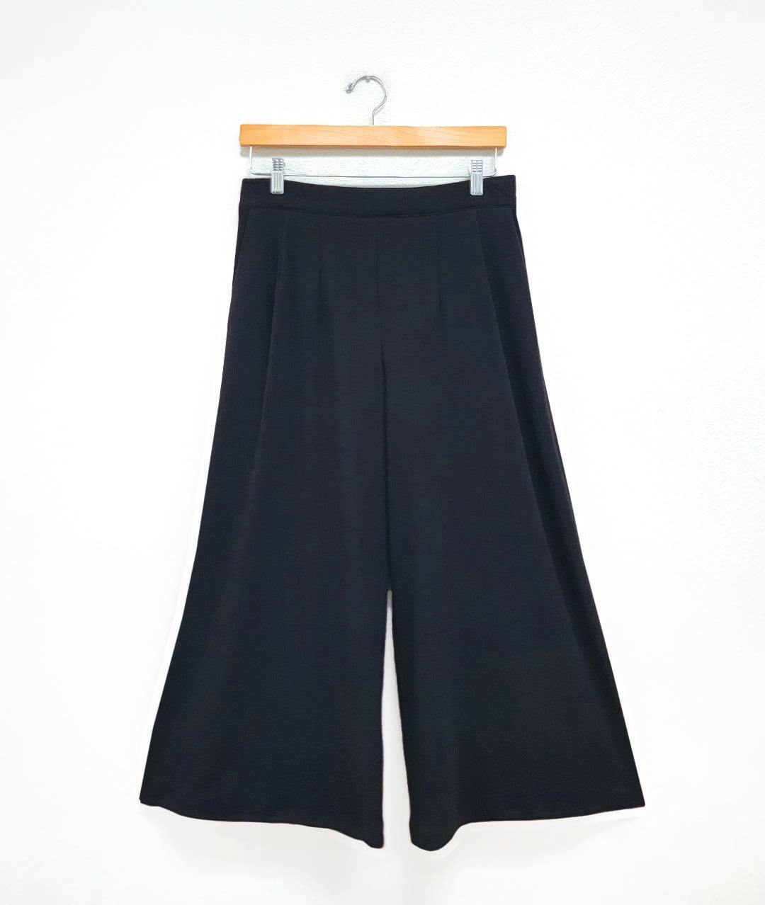 Black wide-leg pants on a wooden hanger against a white background