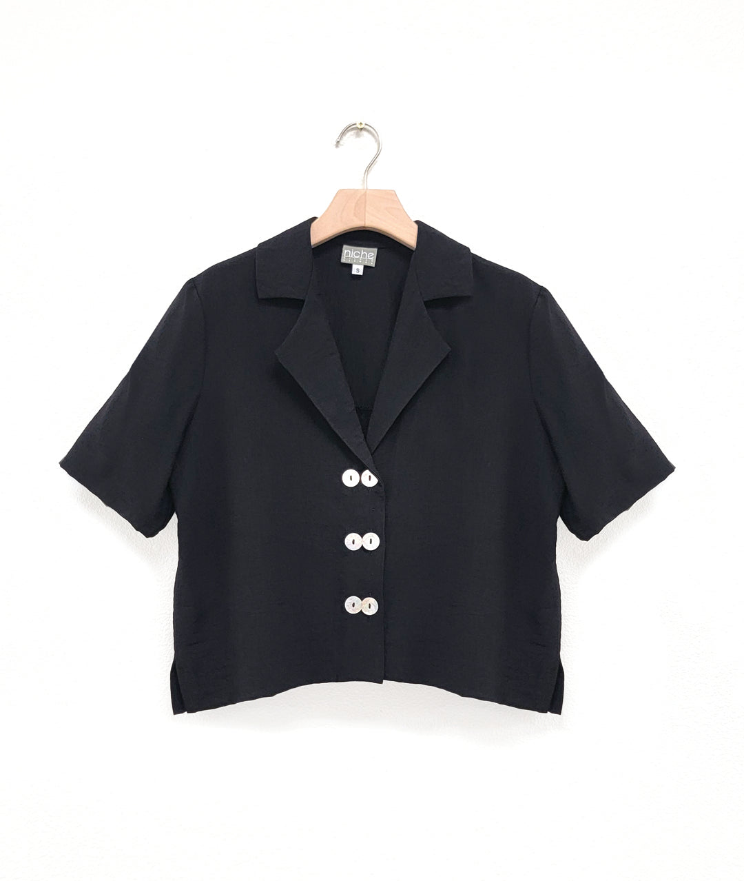 a boxy black button down with an elbow length sleeve and an open collar top has 3 sets of double buttons