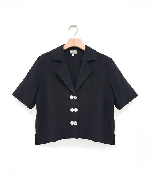a boxy black button down with an elbow length sleeve and an open collar top has 3 sets of double buttons