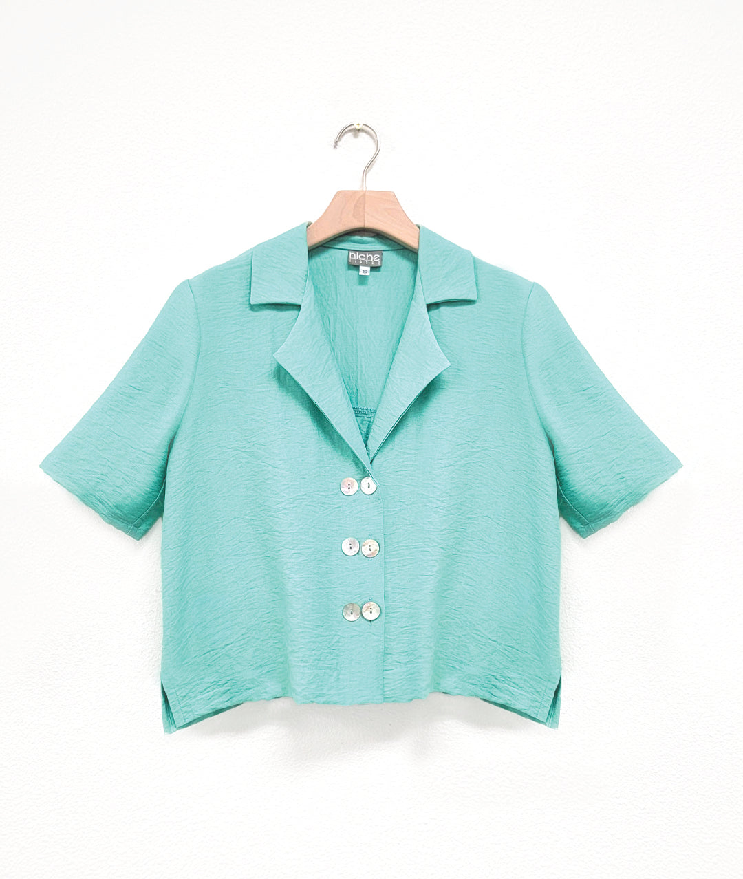 a boxy black button down with an elbow length sleeve and an open collar top has 3 sets of double buttons