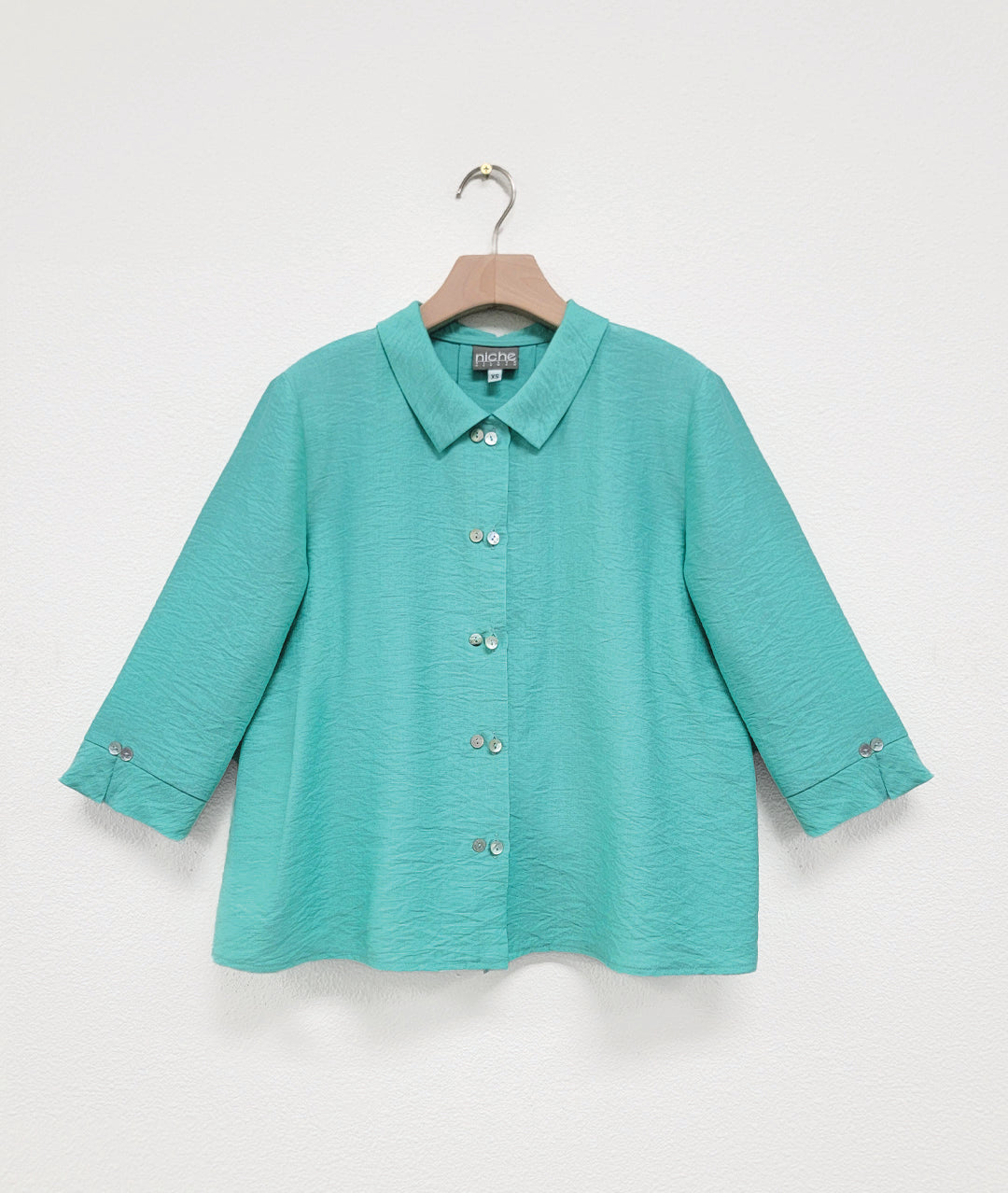 Mint color button up shirt on a hanger against a white background