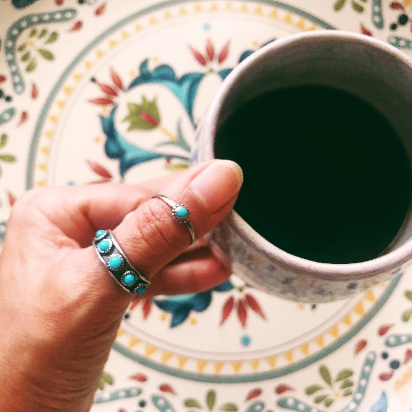 Hand holding a cup of dark liquid on a colorful plate