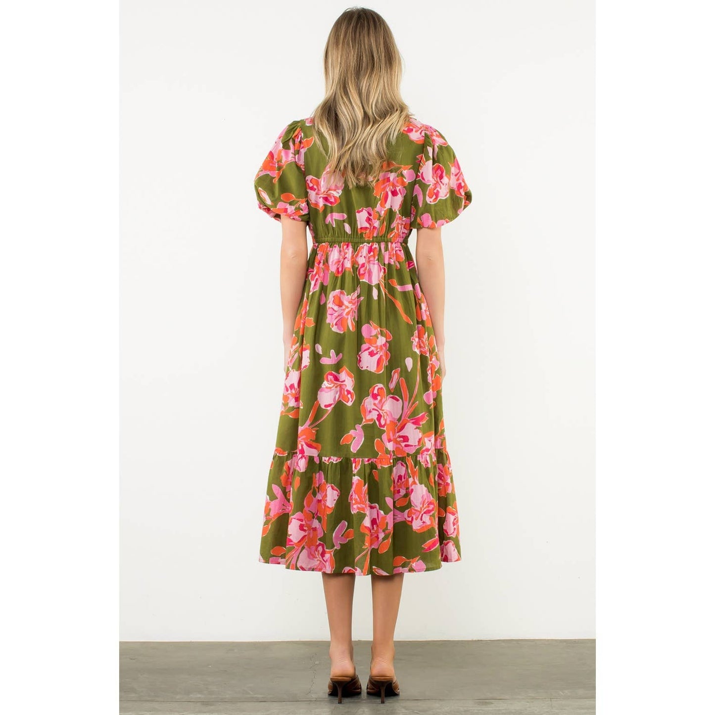 Woman showing back of olive green floral puff sleeve dress with a white background
