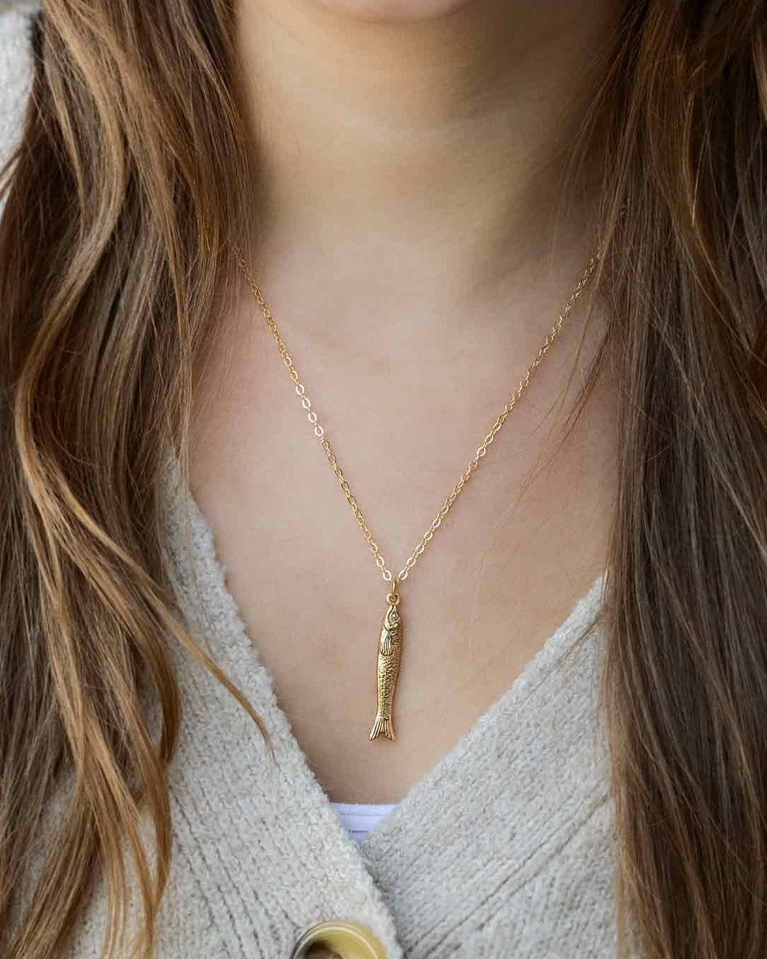 Woman wearing a gold necklace with a fish shaped pendant